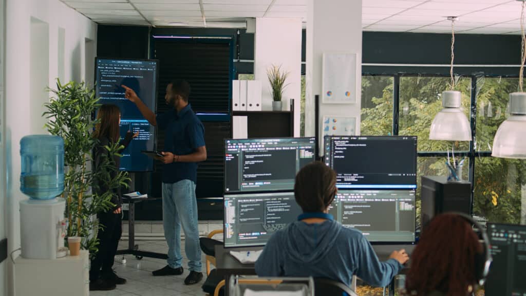 Diverse team of software engineers analyzing code on wall screen tv